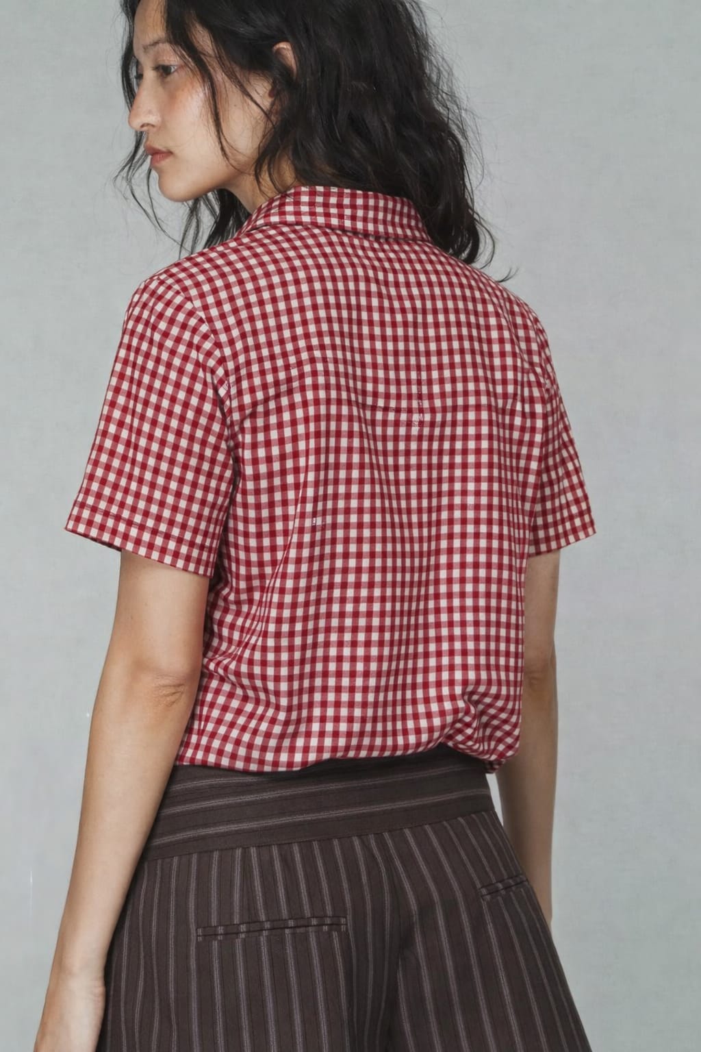 Person wearing a red and white checkered shirt with a plain background