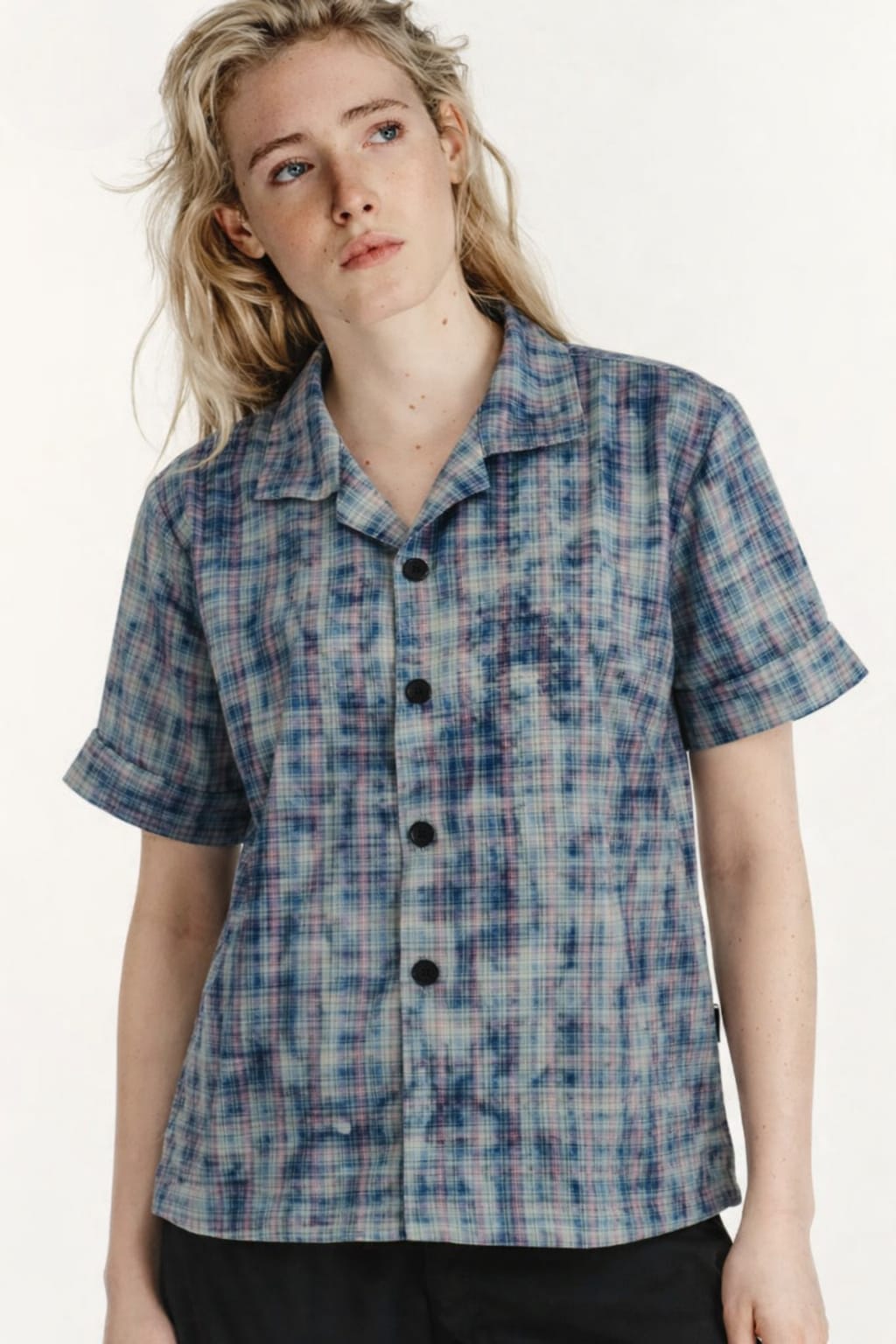 Person wearing a blue plaid shirt with black buttons on a white background