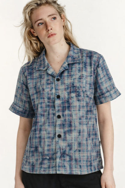 Person wearing a blue plaid shirt with black buttons on a white background