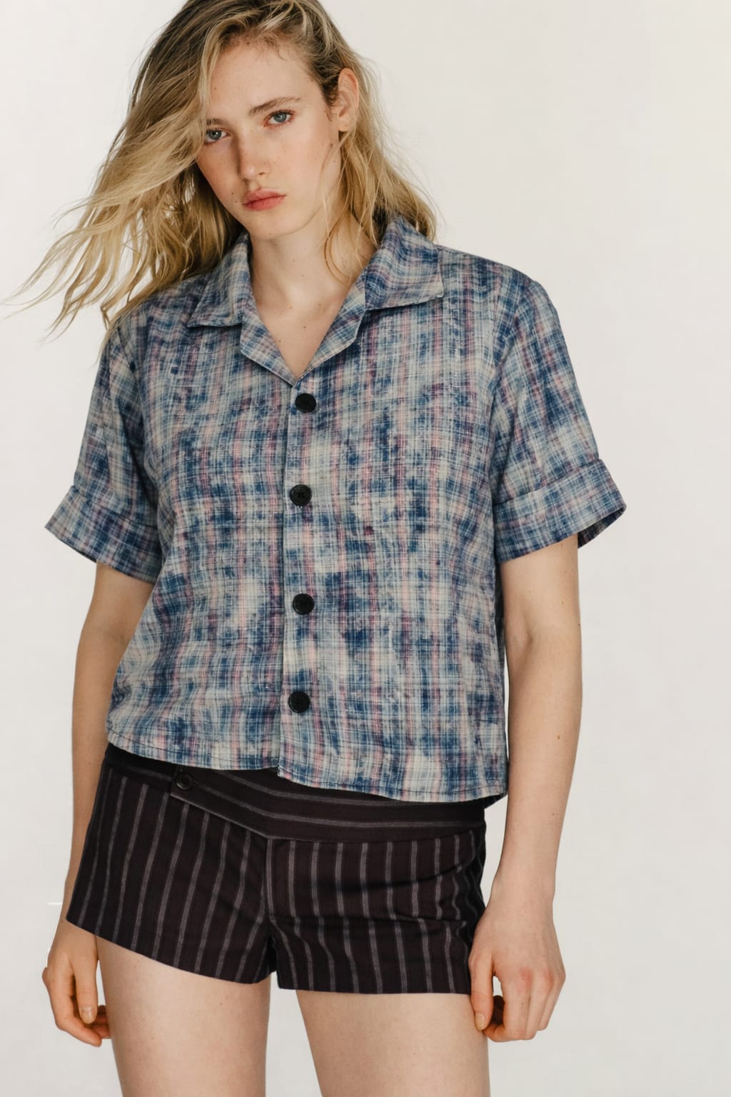 Woman wearing a plaid shirt and striped shorts on a plain background
