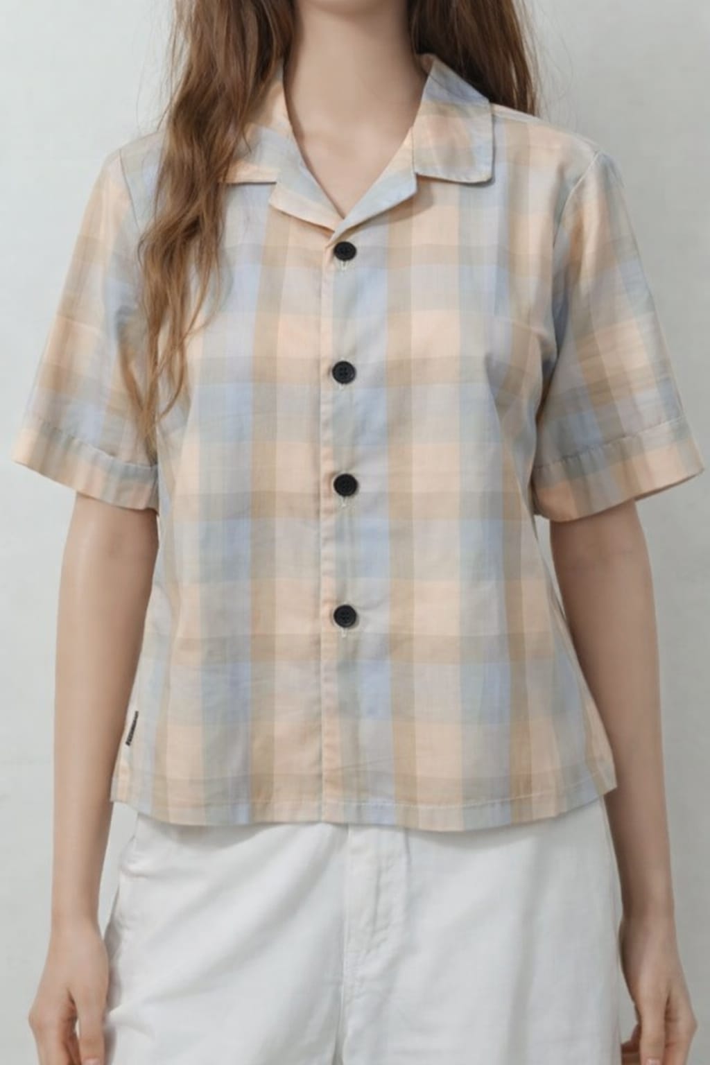Person wearing a plaid shirt with black buttons on a plain background
