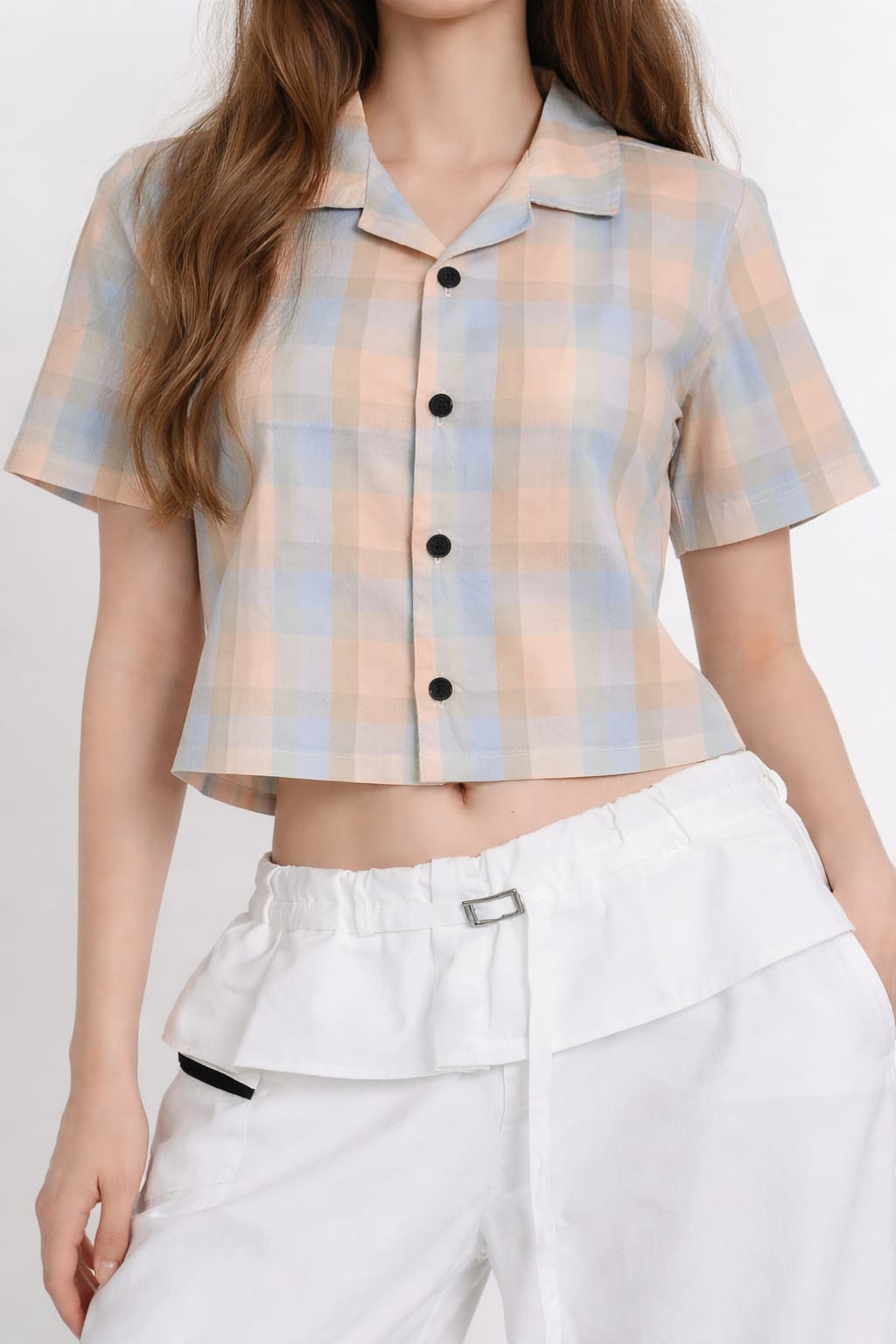 Person wearing a plaid shirt with buttons and white pants on a plain background