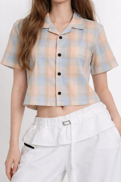 Person wearing a plaid shirt with buttons and white pants on a plain background