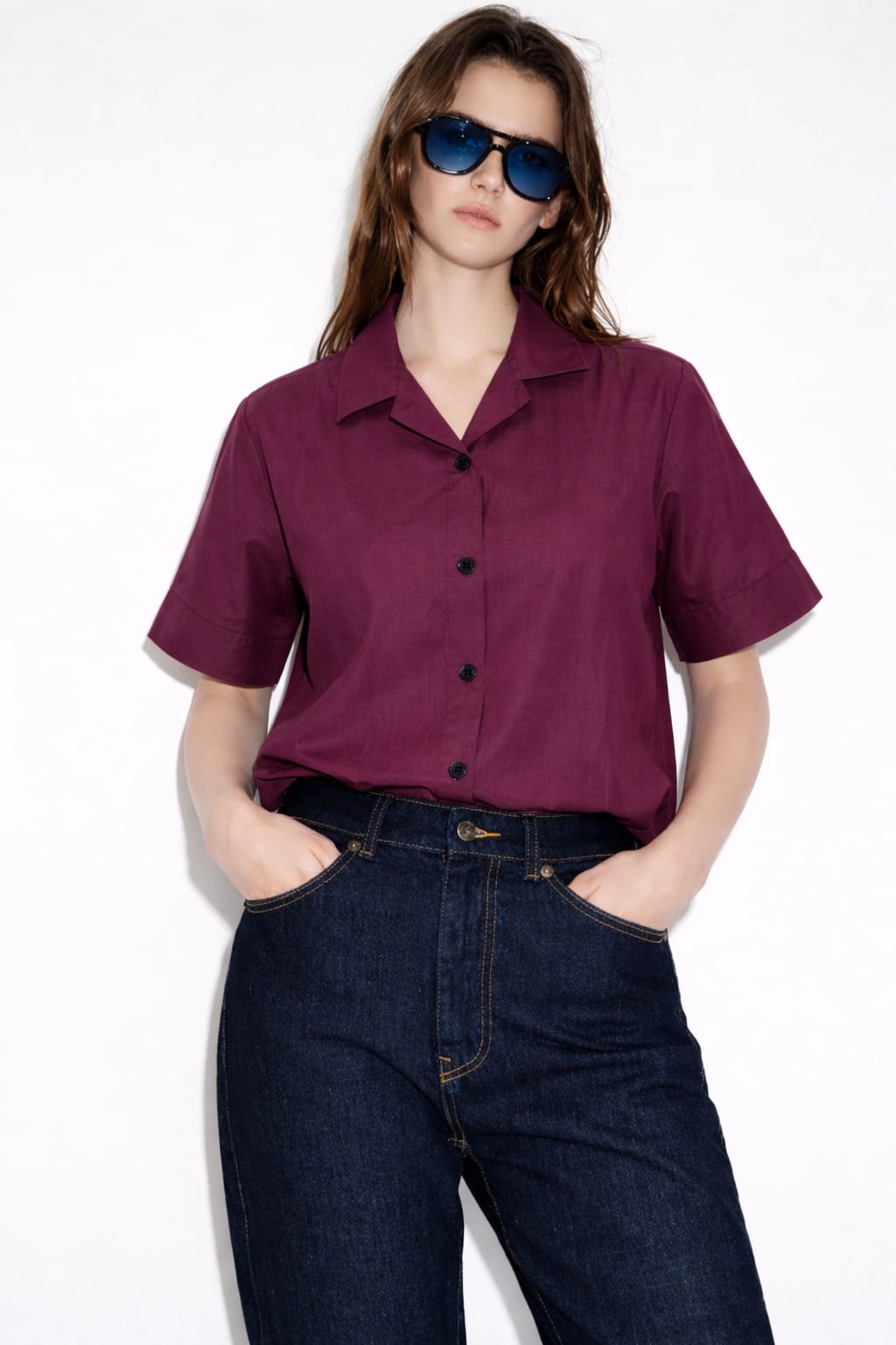 Woman wearing a purple shirt and blue jeans with sunglasses on a white background