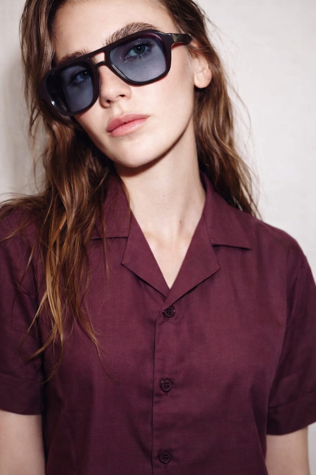 Person wearing sunglasses and a maroon shirt against a plain background