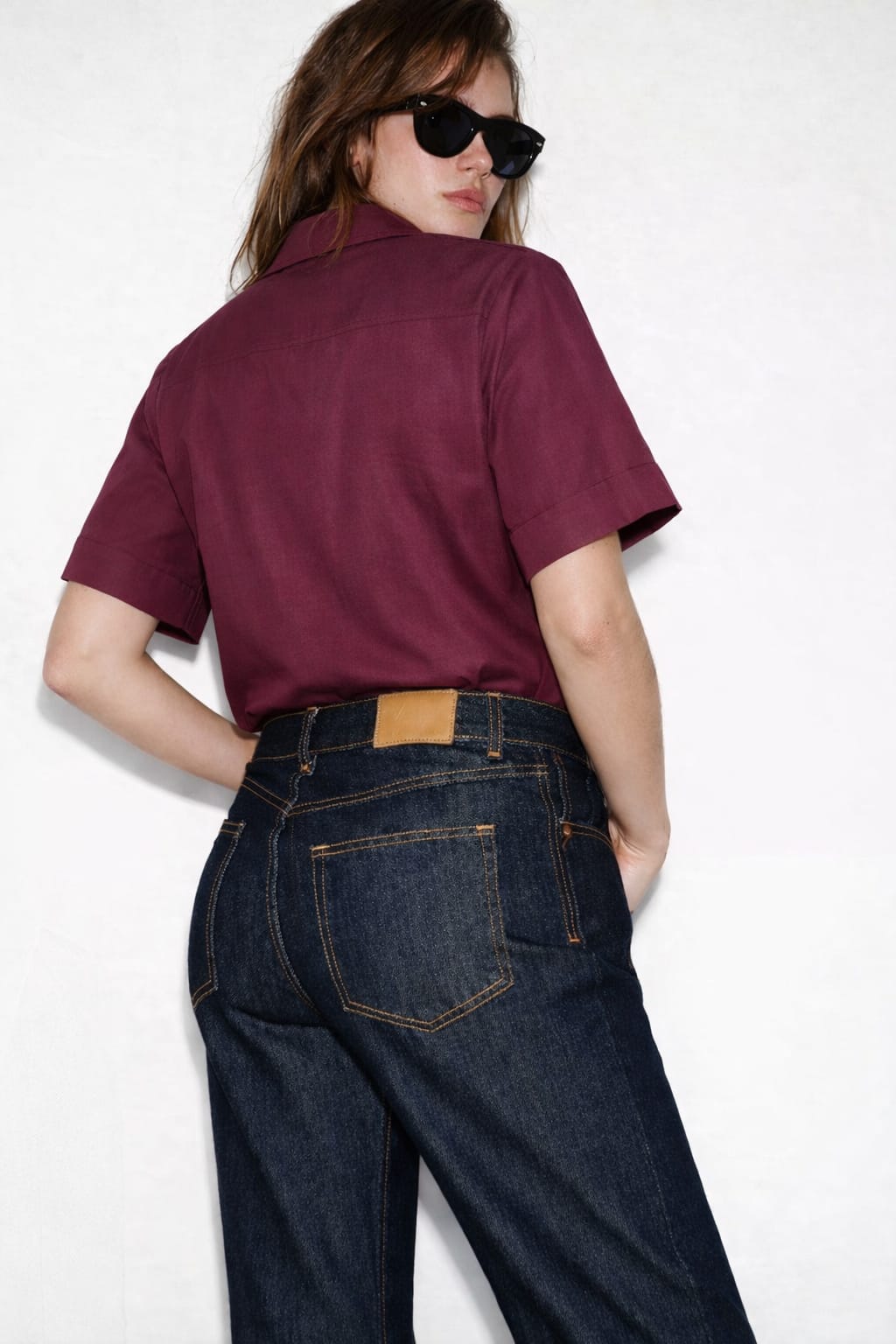 Person wearing a burgundy shirt and blue jeans on a white background