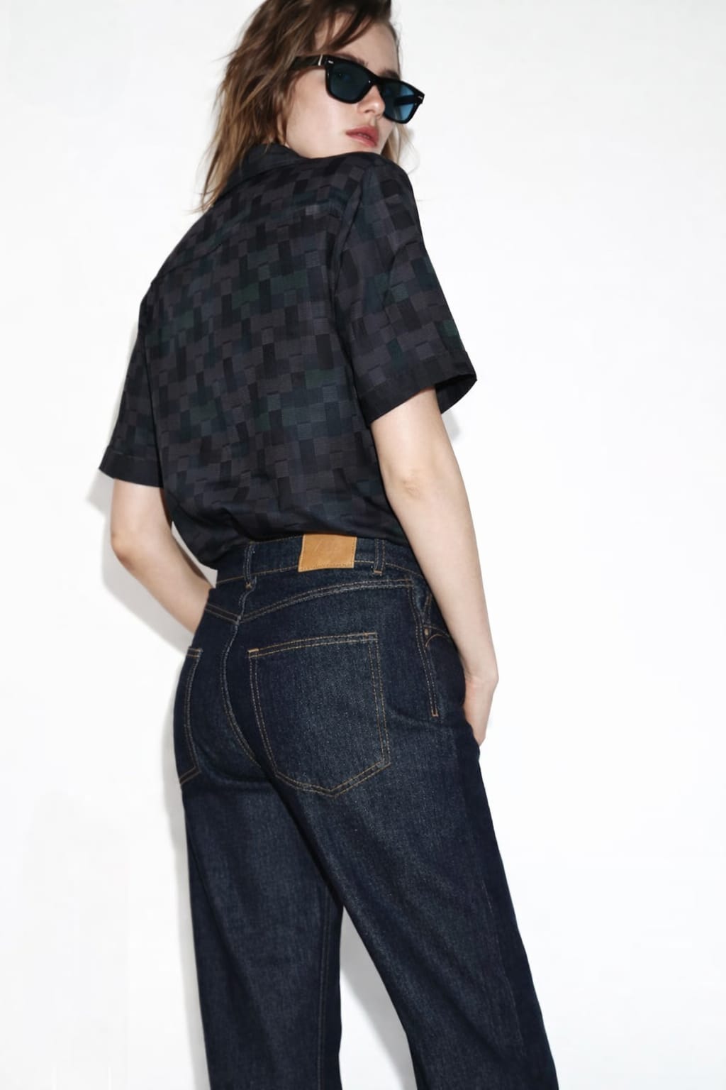 Person wearing a black checkered shirt and blue jeans on a white background