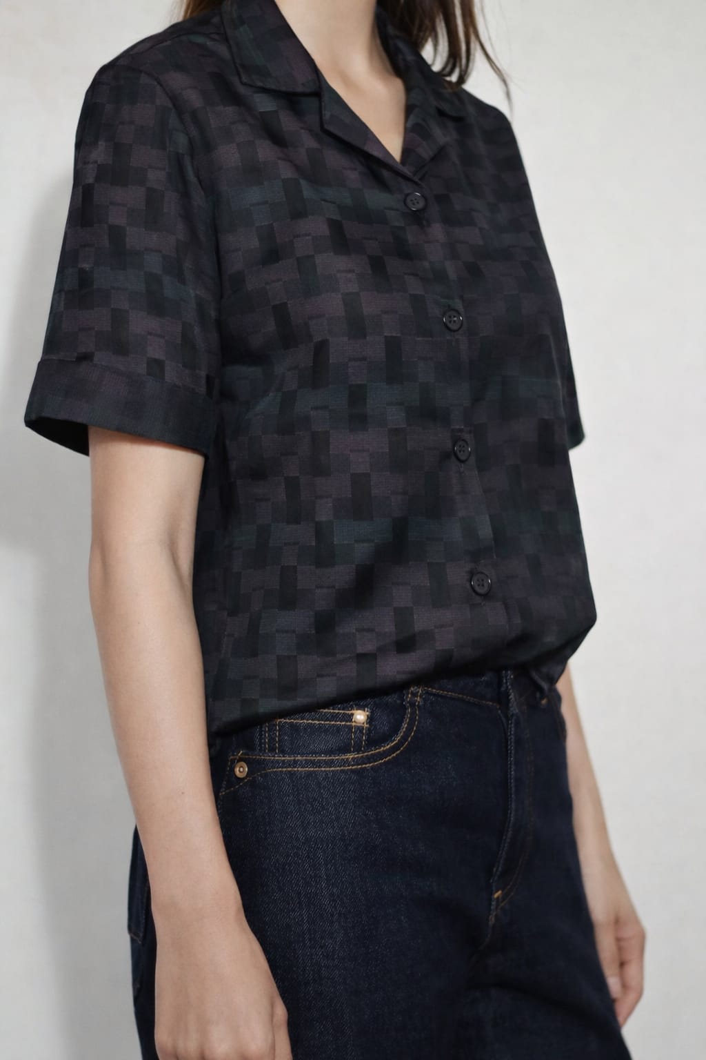 Person wearing a black patterned shirt and dark jeans against a white background