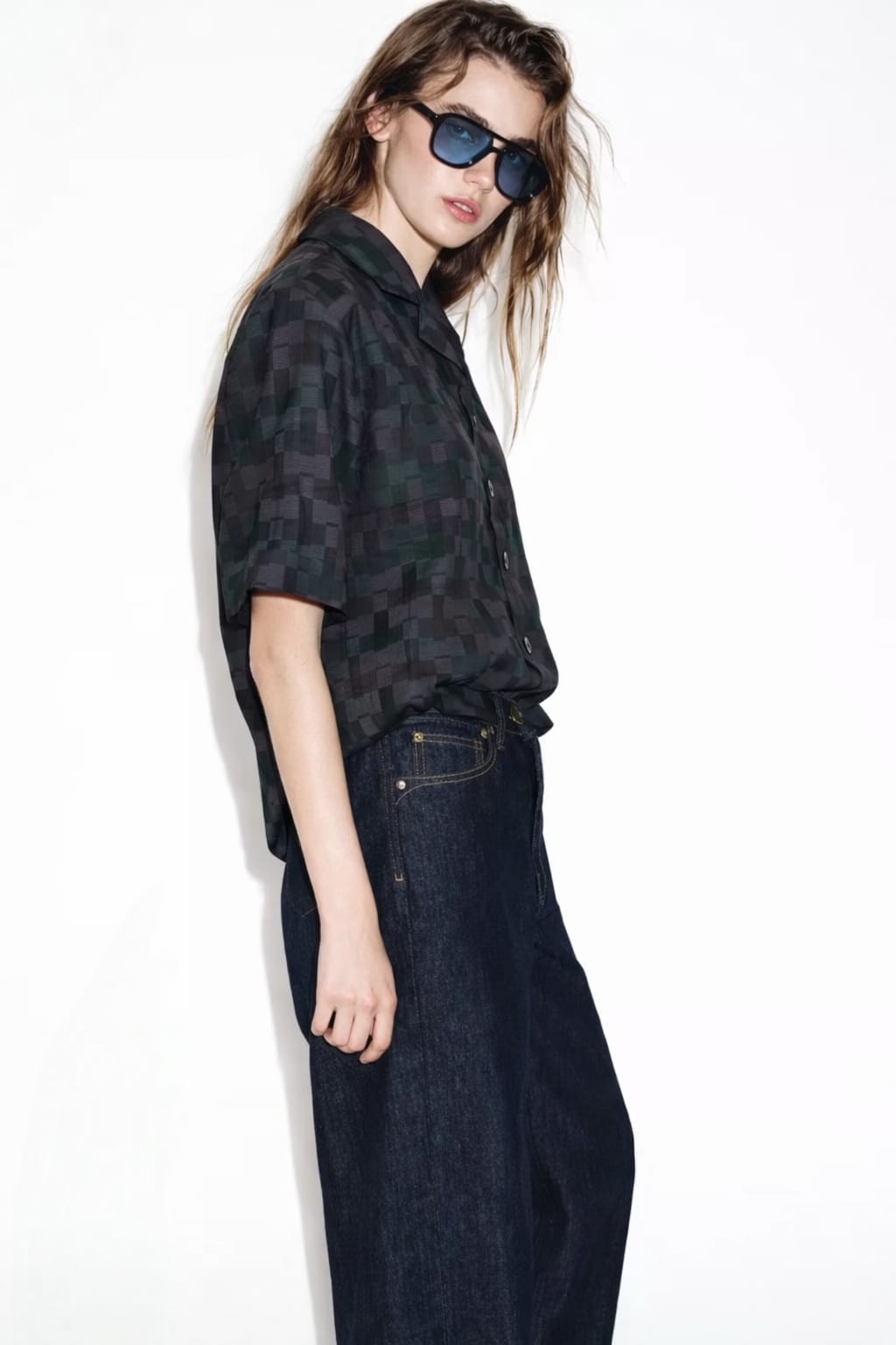 Person wearing a patterned shirt and dark jeans on a white background