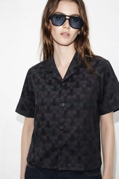 Person wearing a black patterned shirt and sunglasses on a white background