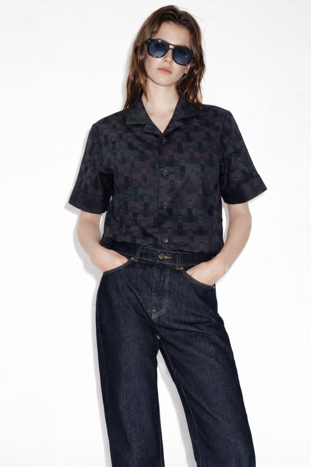 Person wearing a black patterned shirt and blue jeans on a white background