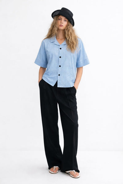 Woman wearing a light blue shirt, black pants, and a black hat on a white background