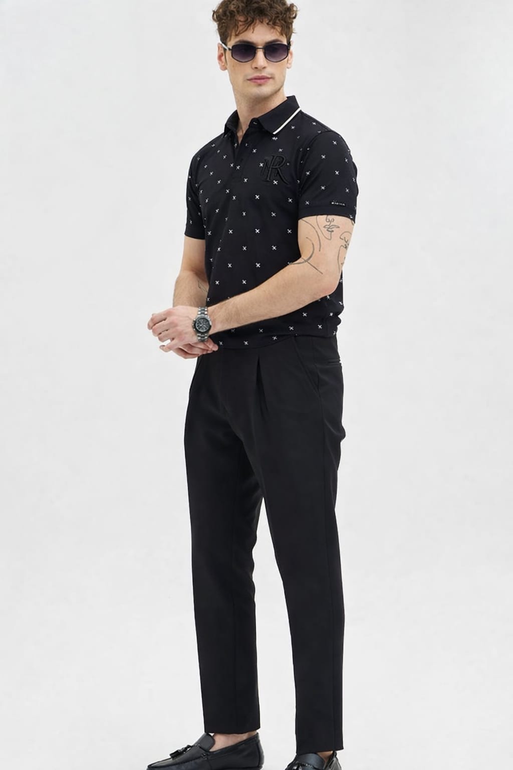 Man wearing a black polo shirt with white patterns and black pants on a light gray background