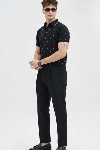 Man wearing a black polo shirt with white patterns and black pants on a light gray background