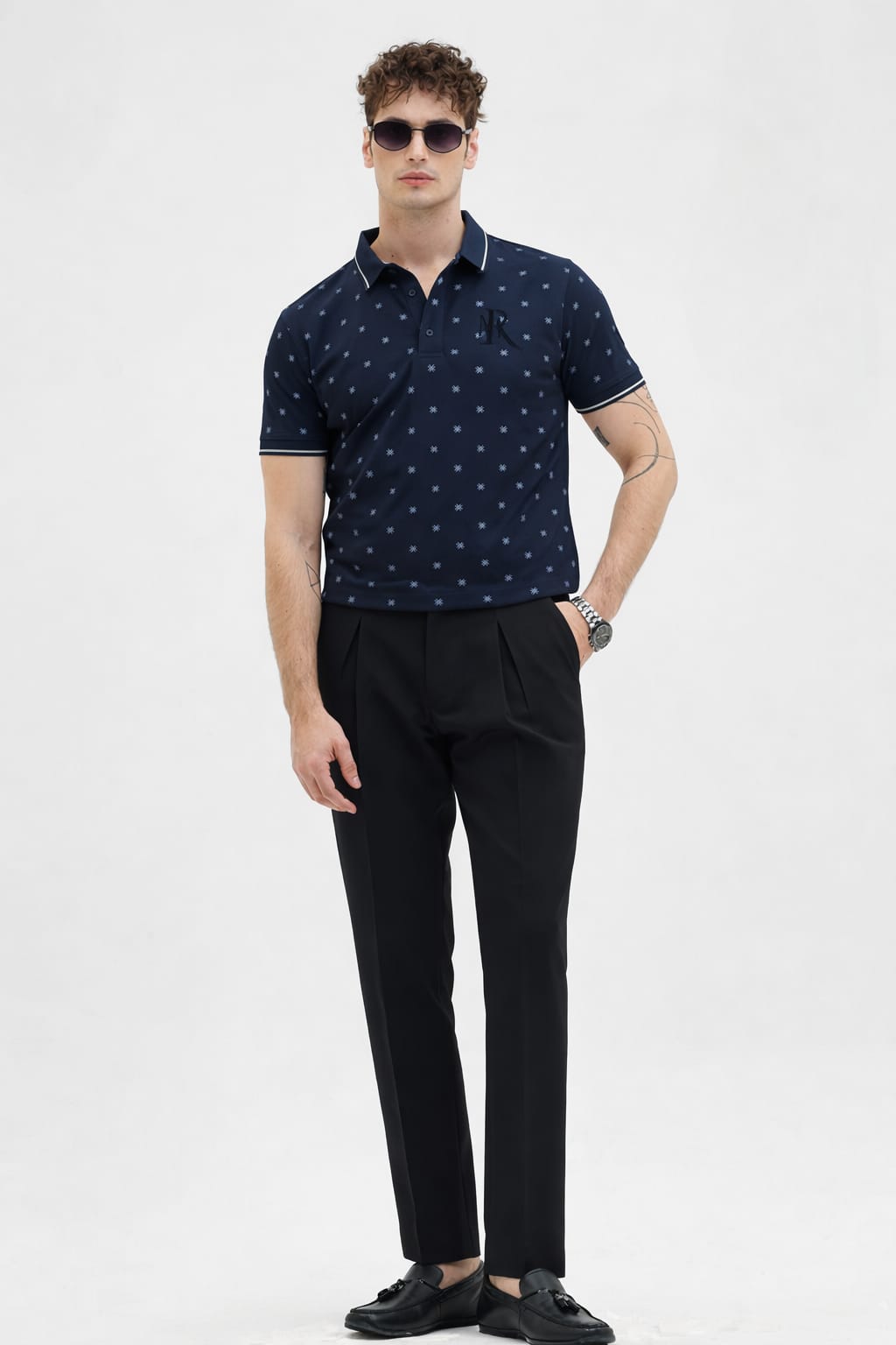 Man wearing a navy polo shirt with white patterns and black pants on a white background