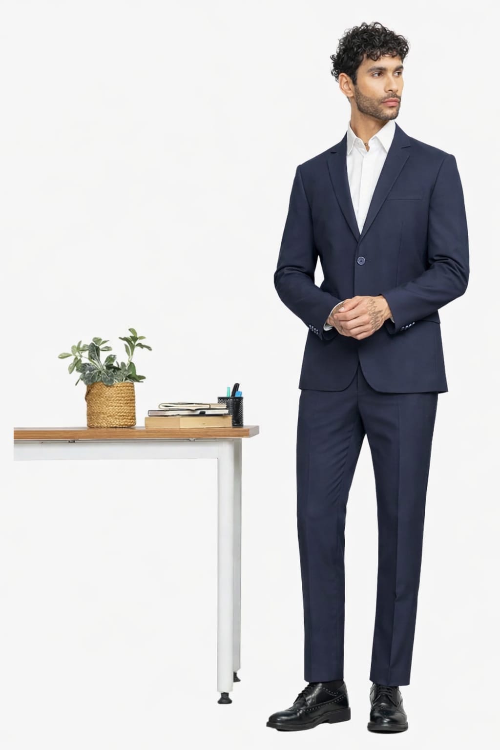 Man wearing a navy suit standing next to a desk with a plant on a white background