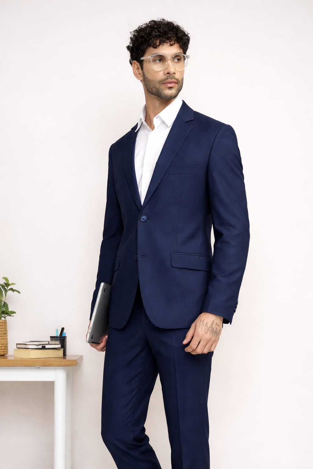 Man wearing a navy blue suit with a white shirt, holding a folder, against a light background.