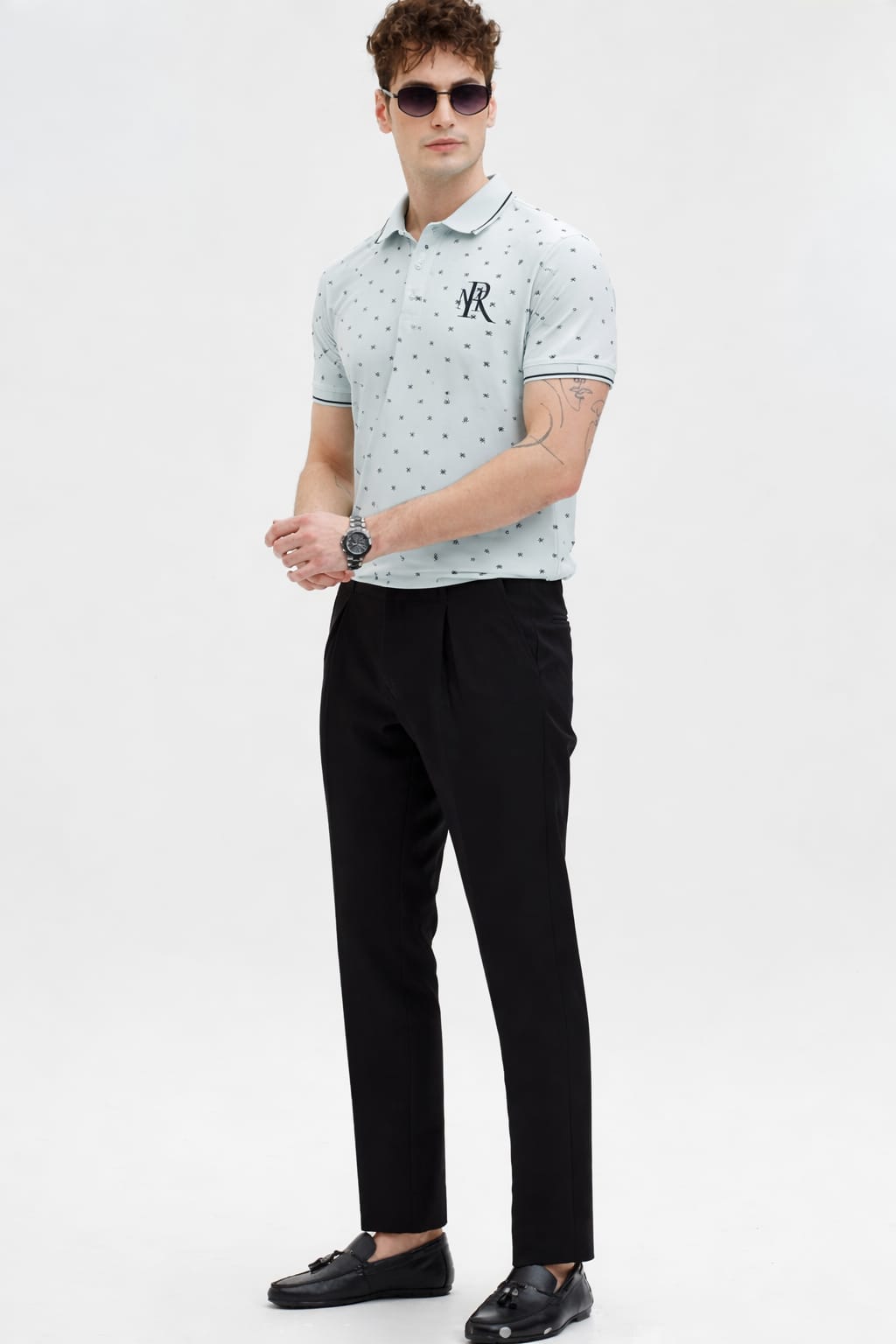 Man wearing a light gray patterned polo shirt and black pants on a white background
