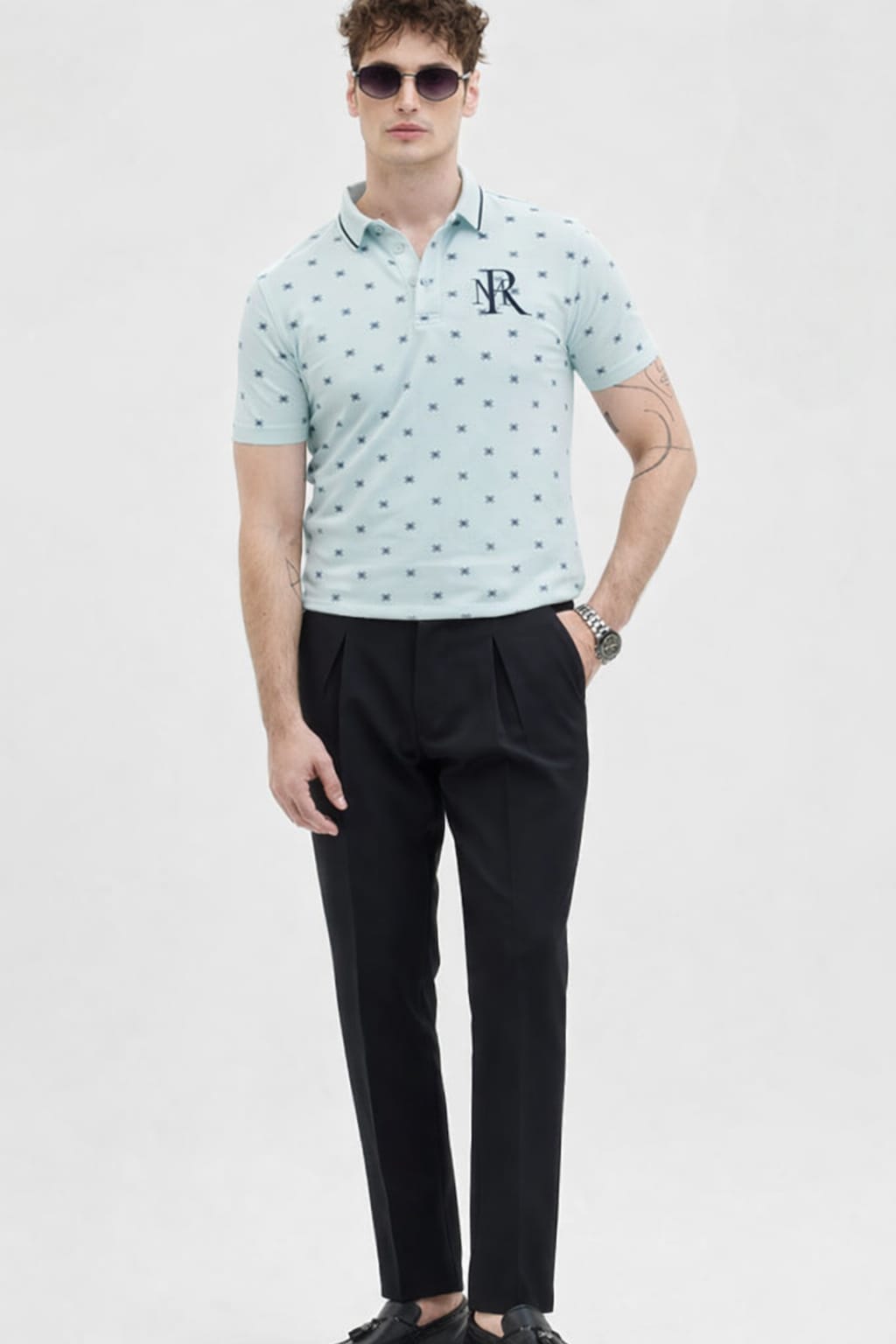 Man wearing a light blue patterned polo shirt and black pants on a white background
