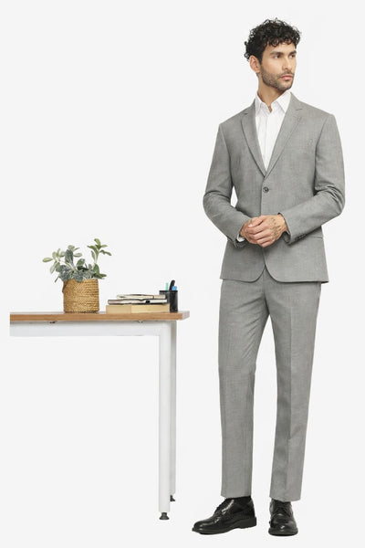Man wearing a gray suit standing next to a white desk with a plant on a white background
