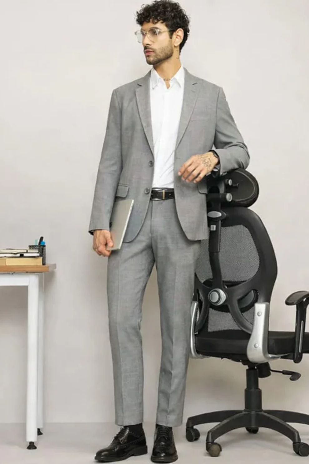 Man in a gray suit standing next to an office chair in an office setting