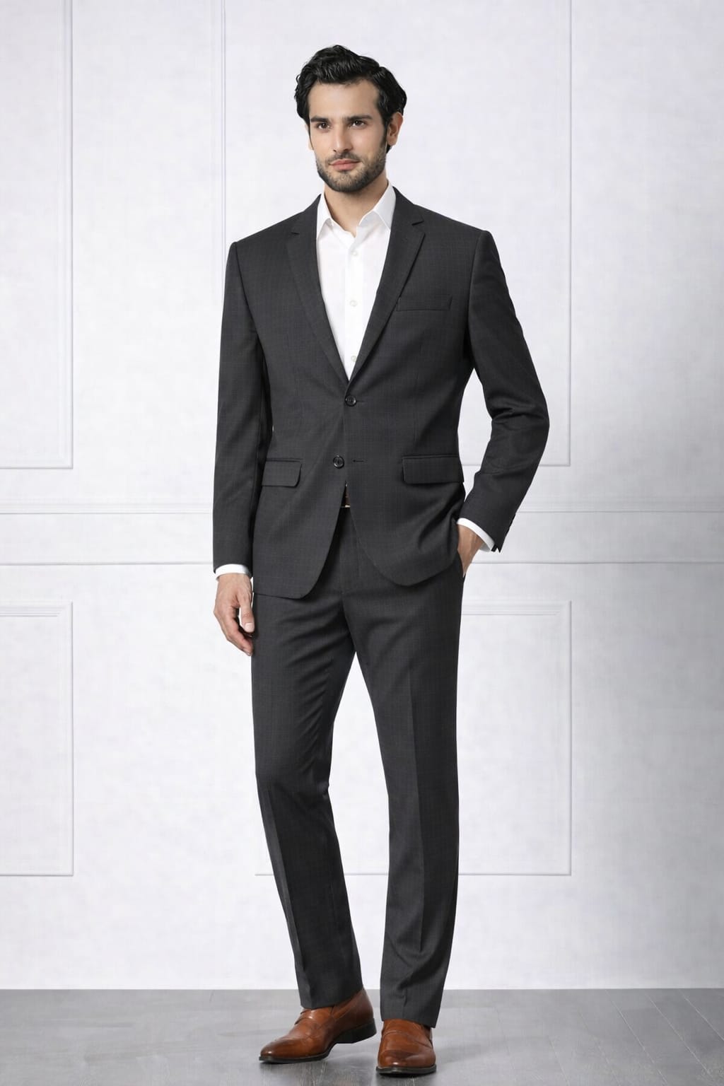Man wearing a dark gray suit with a white shirt and brown shoes against a light gray background