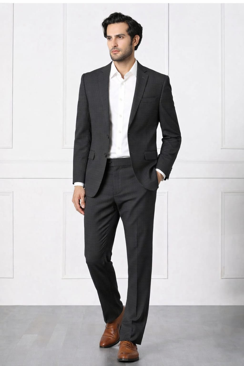 Man wearing a dark gray suit with a white shirt and brown shoes against a white background