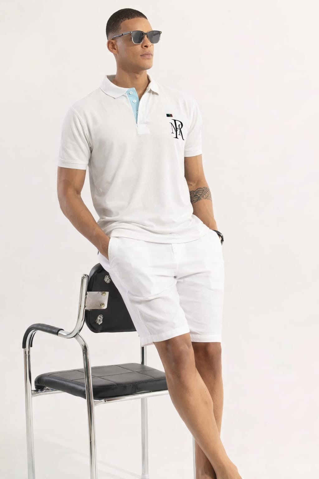 Man in white polo shirt and shorts with sunglasses, leaning against a chair on a white background