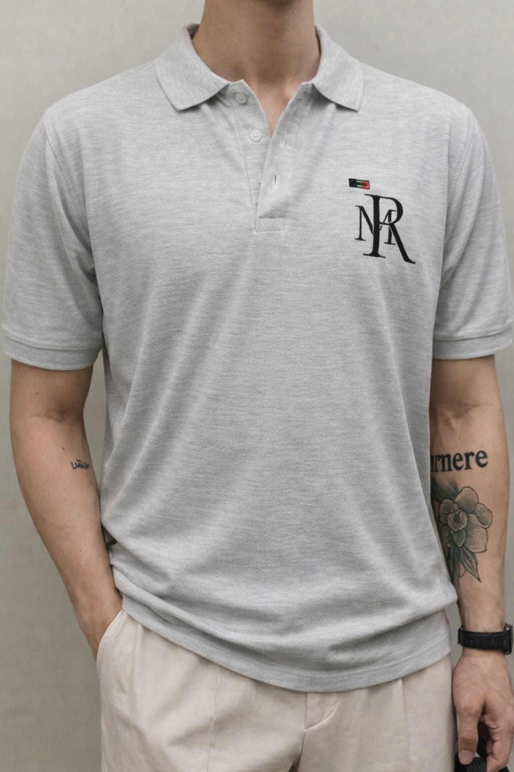 Person wearing a gray polo shirt with a logo on a plain background