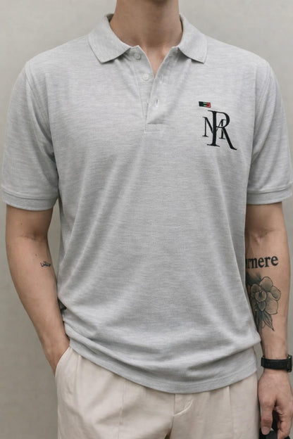 Person wearing a gray polo shirt with a logo on a plain background