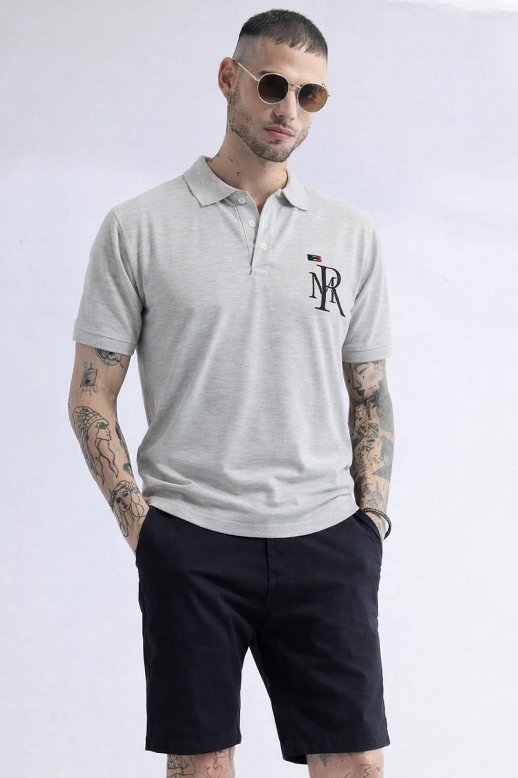 Man wearing a gray polo shirt with a logo and black shorts on a white background