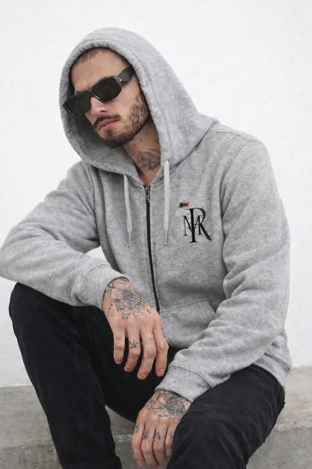 Man wearing a gray hoodie with a logo, sitting against a white background
