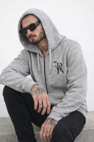 Man wearing a gray hoodie with a logo, sitting against a white background