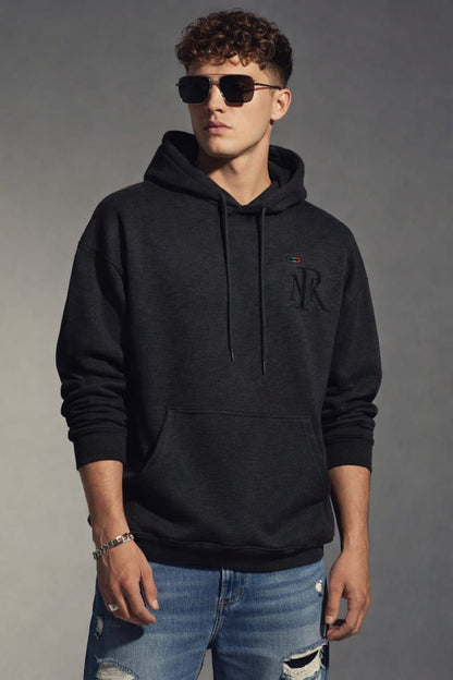 Man wearing a black hoodie with a logo and sunglasses, standing against a gray background