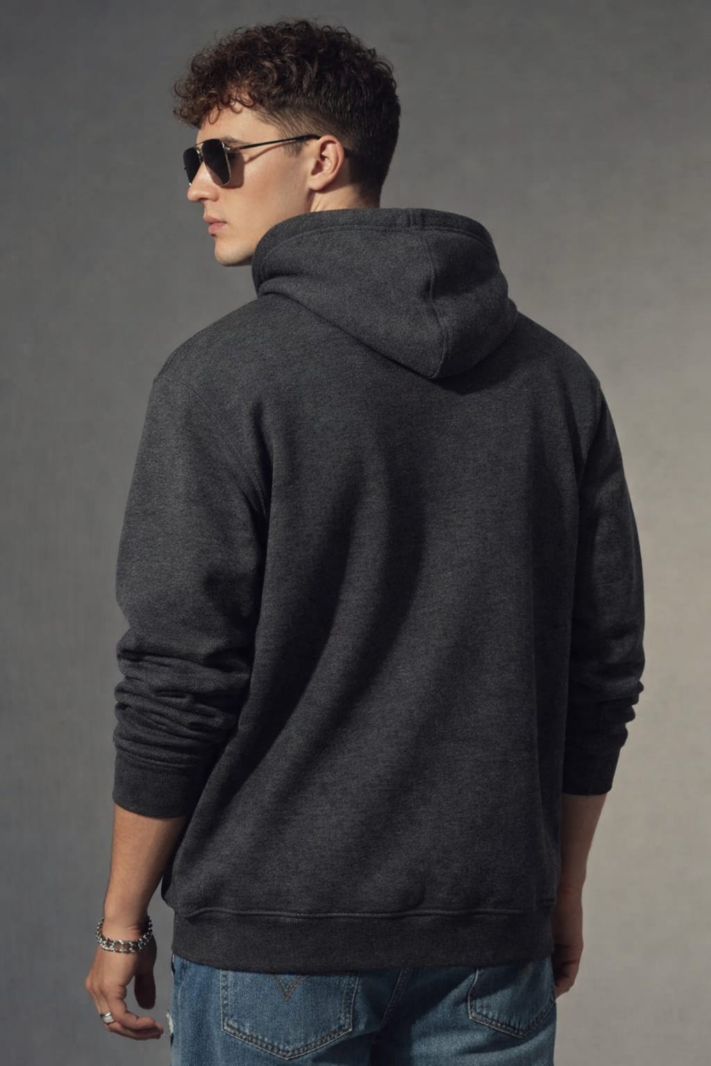 Person wearing a dark gray hoodie and sunglasses, standing against a plain background