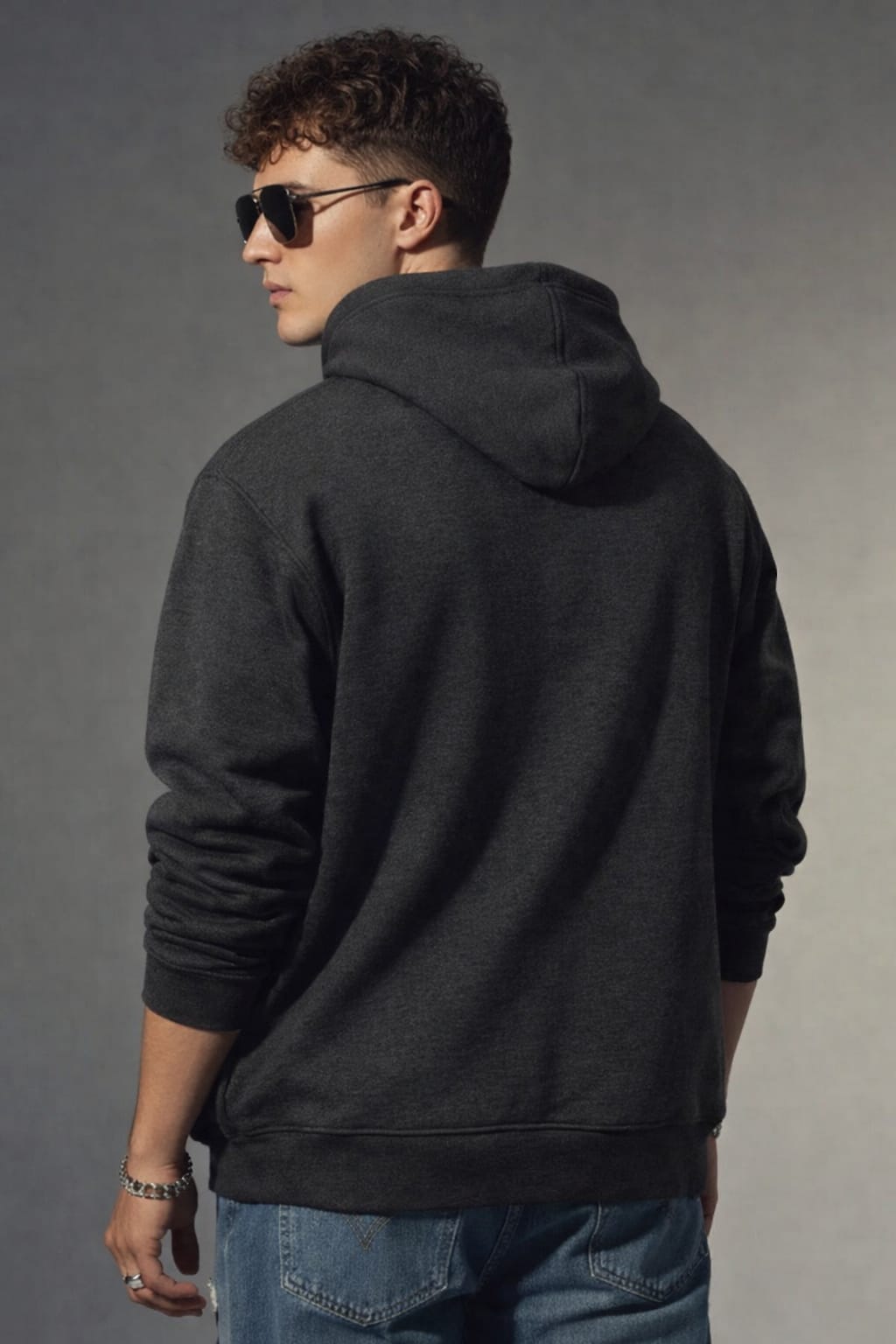 Person wearing a black hoodie and sunglasses, standing against a gray background