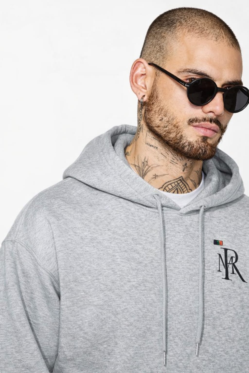 Man wearing a gray hoodie with a logo, sunglasses, and visible tattoos on a white background