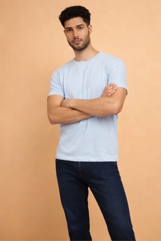 Man wearing a light blue t-shirt and dark jeans against a beige background