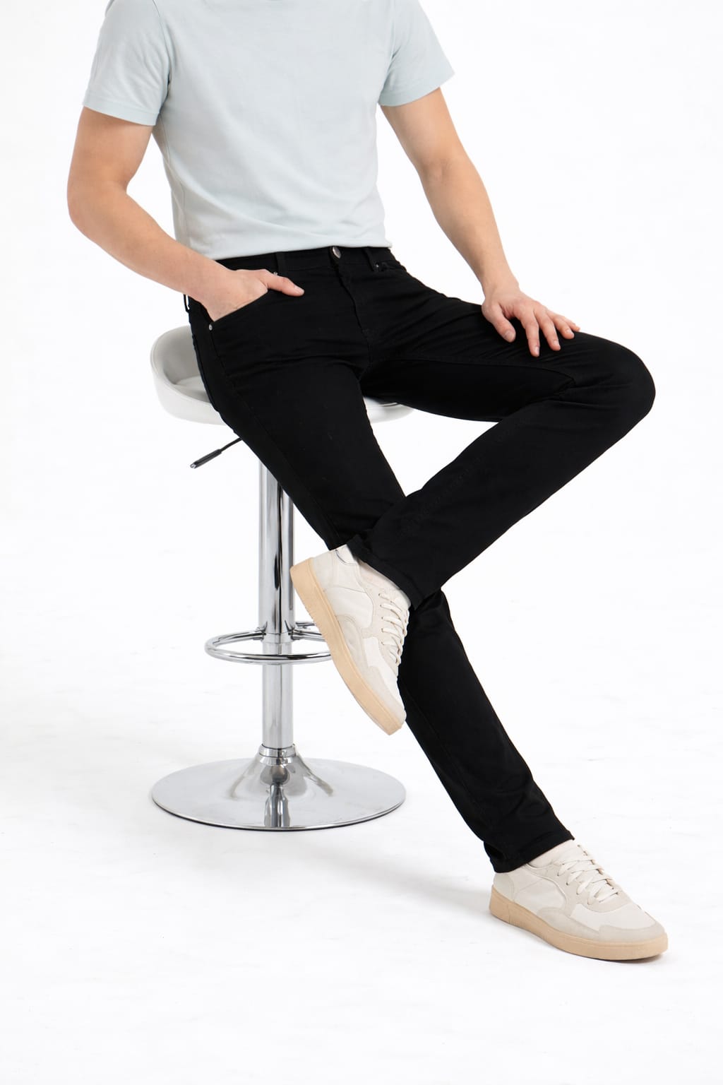 Person wearing black pants and white sneakers sitting on a bar stool against a white background