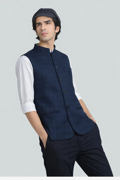 Man wearing a navy blue vest over a white shirt with a gray background