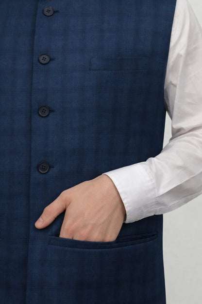 Navy blue vest with buttons and a white shirt sleeve on a plain background