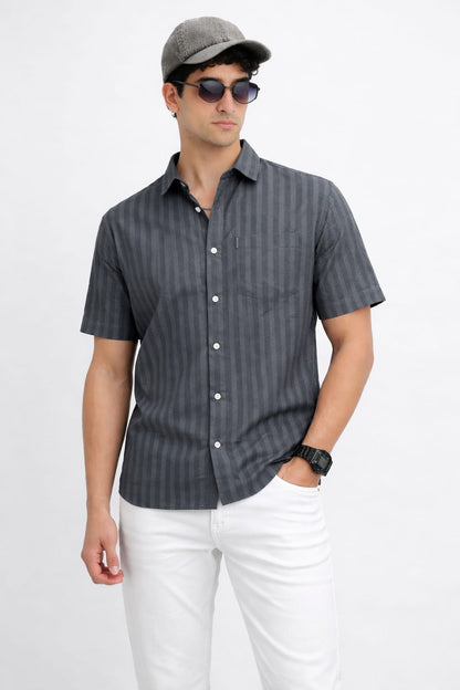 Man wearing a gray striped shirt, white pants, and a cap with sunglasses on a white background