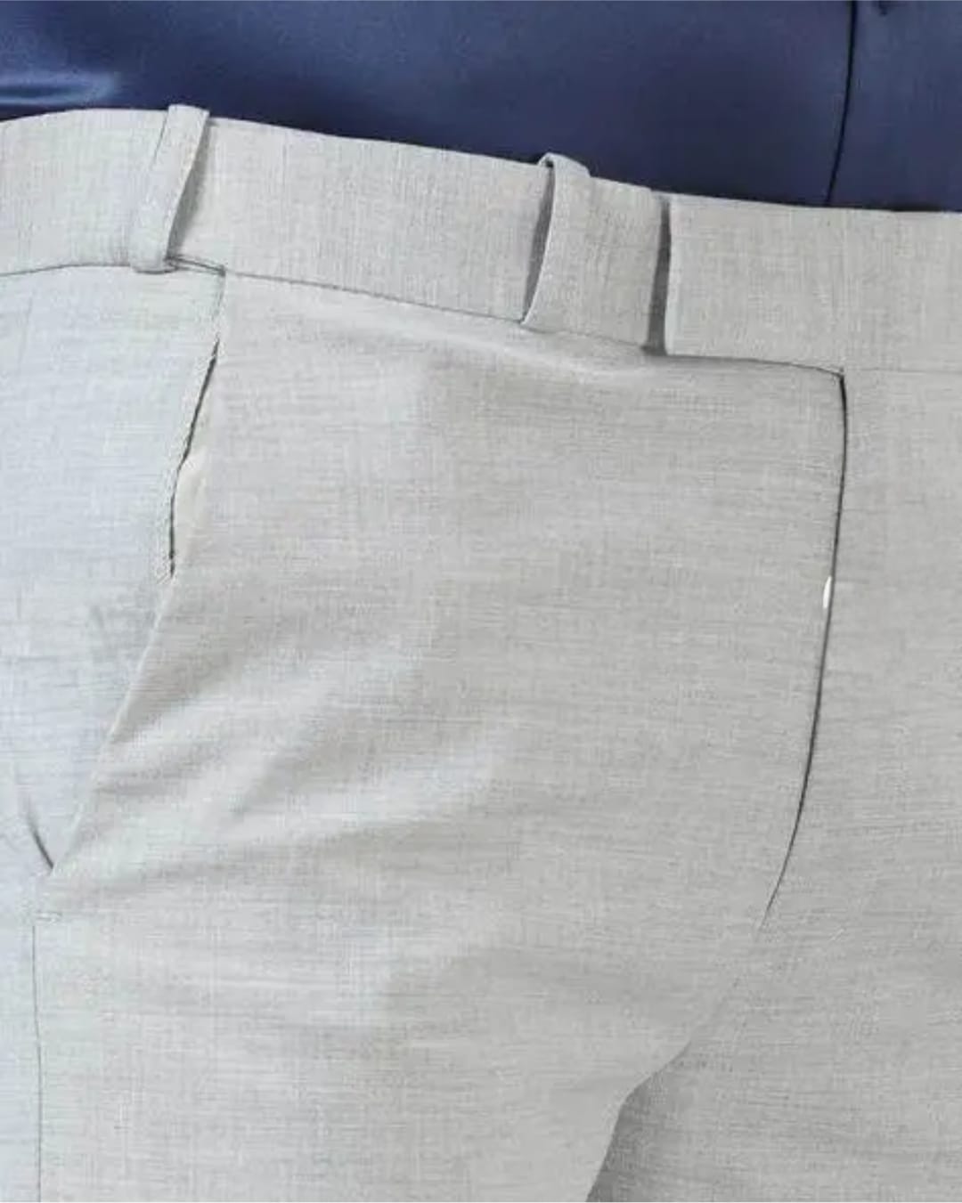 Close-up of light gray pants with a blue background