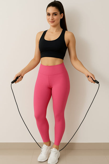 Woman in black sports bra and pink leggings holding a jump rope against a plain background