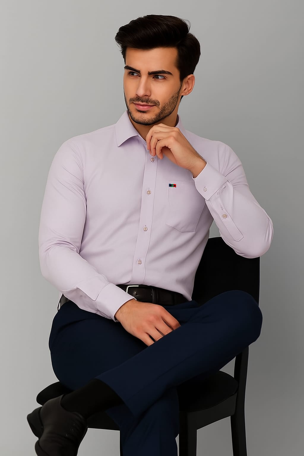 Man wearing a light purple dress shirt and dark pants sitting on a chair against a gray background