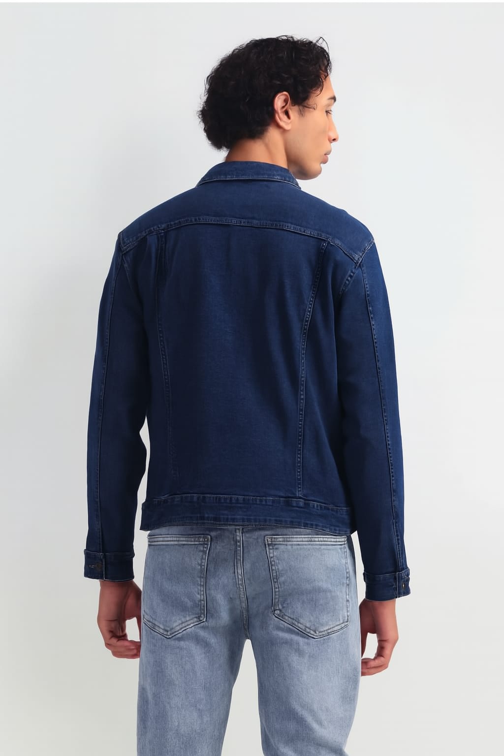 Person wearing a blue denim jacket and jeans on a white background