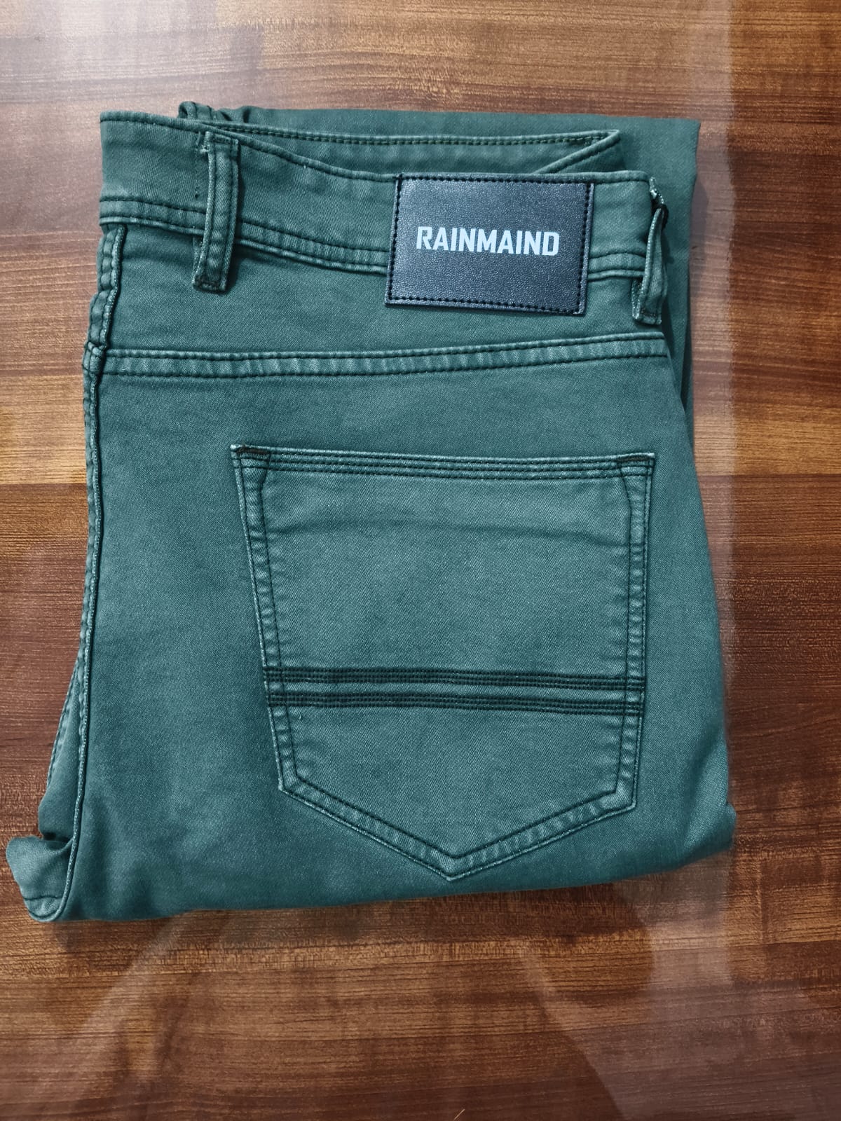 Folded green jeans with 'Rainmaid' label on a wooden surface