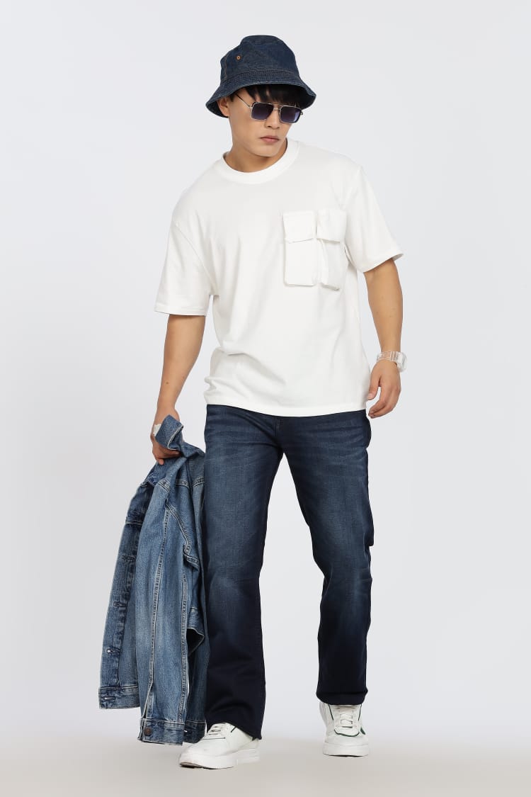 Person wearing a white t-shirt, blue jeans, and a navy bucket hat on a plain background