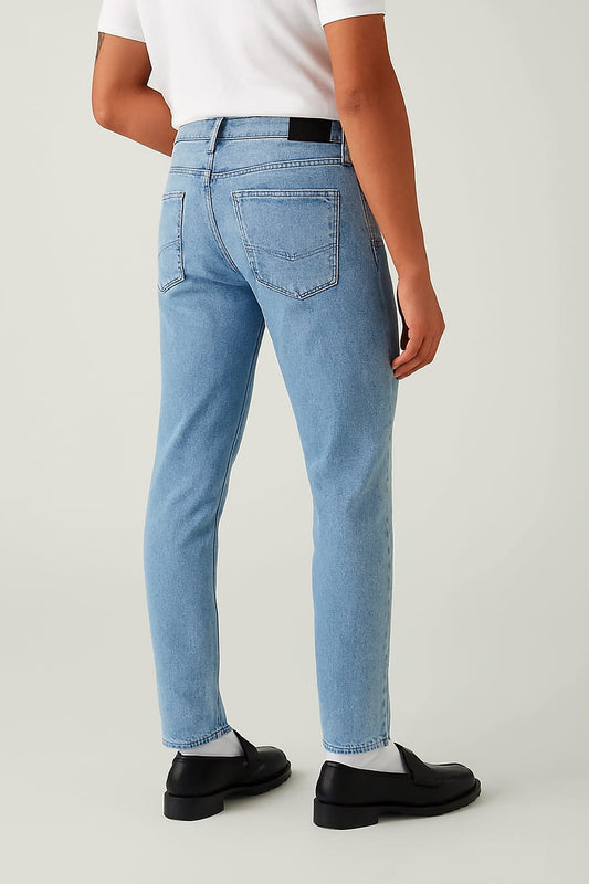 Person wearing light blue jeans and black shoes on a plain background