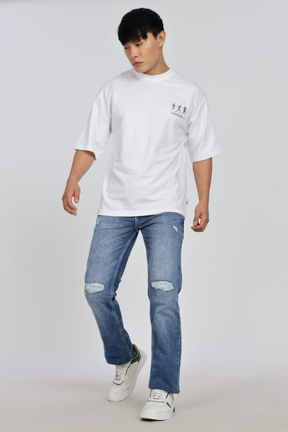 Person wearing a white t-shirt and blue jeans sitting on a white cube.